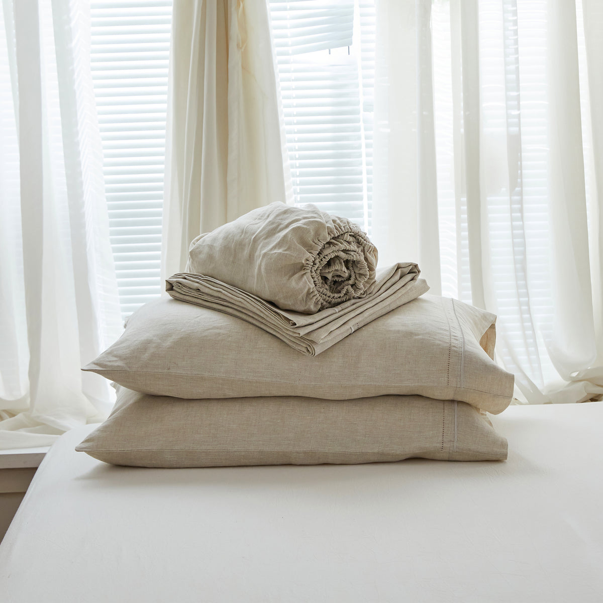 Folded natural-toned bedding and pillows arranged in soft window light